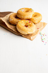 Top view of several classic donuts with colored noodles, on brown paper and table, on white table, in vertical, with copy space