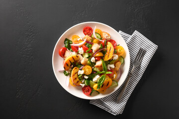 Piquant Panzanella with tomatoes, bread, cheese and peach in white plate on black background. Top view. Traditional Italian cuisine. Vegetarian panzanella salad. Mediterranean healthy food.