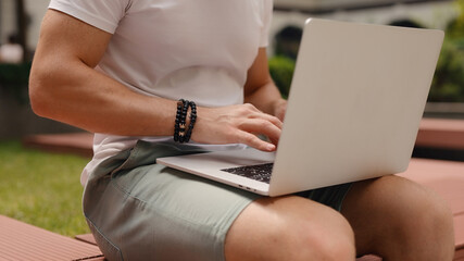 Naklejka premium Closeup unrecognizable man using laptop sitting at the yard of business center