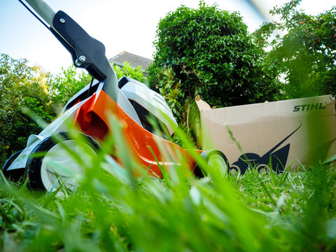 Paris, France - Jun 12, 2021: Unboxing Low angle view of new Stihl lawn mower operated with li-ion batteries - after unboxing with beautiful rustic cottage house in background