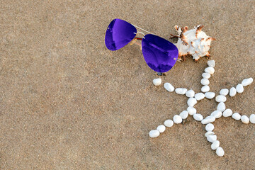 Blue sunglasses lie on sand beach with seashell and sun made of white stones. Concept summer holiday with copy space, protection from sun, holidays at sea, trip to ocean. Beach accessories on sand.
