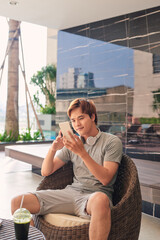 A young asian man is relaxing near the outdoor pool with a book in his hands.