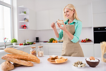 Photo of dreamy gorgeous nice looking smiling mature woman spread butter on break prepare homemade sandwich at home