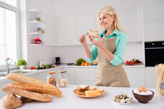 Photo of dreamy gorgeous nice looking smiling mature woman spread butter on break prepare homemade sandwich at home