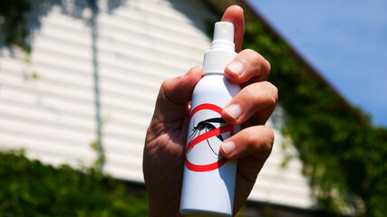 Close-up of the mosquito spray in a male hand against a summer house background