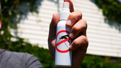 Close-up of the mosquito spray in the hand of a man against a summer house background