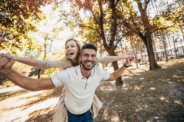 Boyfriend carrying his girlfriend on piggyback in autumn park.