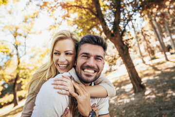 Boyfriend carrying his girlfriend on piggyback in autumn park.