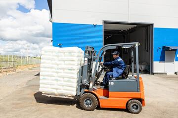 A man on a forklift works in a large warehouse, unloads bags of raw materials