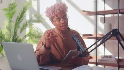 African American woman in front of a microphone reads on a digital tablet during a podcast. Young...