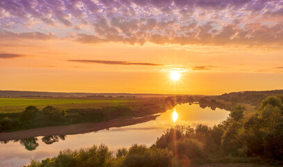 Fototapeta na wymiar amazing view at beautiful summer river sunset, halo with reflection on water with green bushes, calm water ,deep colorful cloudy sky and glow on horizon on a background, spring evening landscape