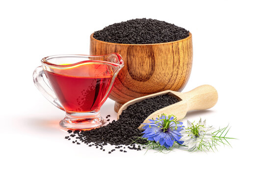 Black cumin oil in gravy boat and nigella sativa flowers. Nigella sativa seeds in wooden scoop isolated on white background.