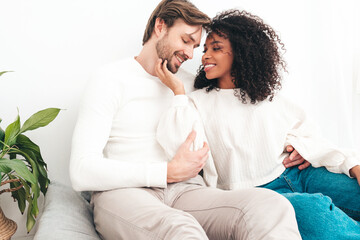 Smiling beautiful woman and her handsome boyfriend. Happy cheerful multiracial family having tender moments. Multiethnic models lying in bed and hugging in white interior. Embracing each other