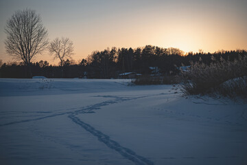 human footprints on snow and ice covered river. Winter evening in Latvia. Sunset in christmas time. Village houses in distance