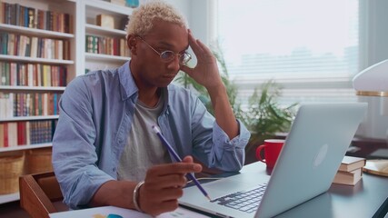 Frustrated sad young afro american businessman looking at laptop screen and holding his head with his hand feeling stressed and depressed. Man in office reads bad news, bank debt reports or bankruptcy