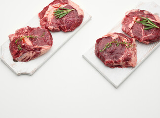 raw piece of beef ribeye with rosemary, thyme on a white table, top view