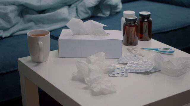 Close up of table with tissues, medication and tea in empty space. Nobody in room with bottles of pills, capsule tablets, medicaments, drugs, drink, and thermometer for ill person