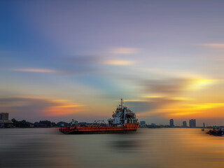 Fototapeta premium A large cargo ship in the middle of the river with beautiful sky during sunset time.