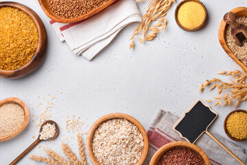 White, brown and red rice, buckwheat, millet, corn groats, quinoa and bulgur in wooden bowls on the light gray kitchen table. Gluten-free cereals. Top view with copyspace