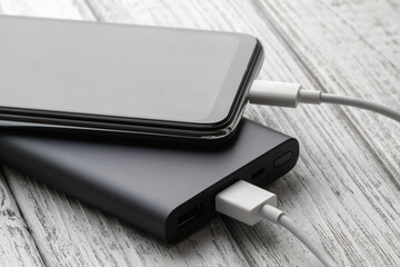 The smartphone is charging from external powerbank with cable on a gray wooden background. Closeup, selective focus