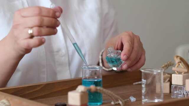 Close-up of a pipette with oil and a glass bottle. woman pouring perfume in bottle. Perfume creating workshop
