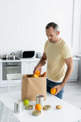 Man taking fruits from paper bag on table in kitchen