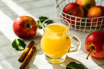 Frischer Apfelsaft in einem Trinkglas und rote Äpfel auf einem weißen rustikalen Tisch. Gesunde Ernährung.