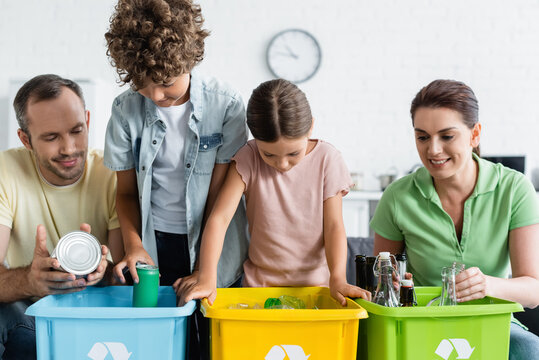 Family with kids sorting trash in boxes with recycle sign at home