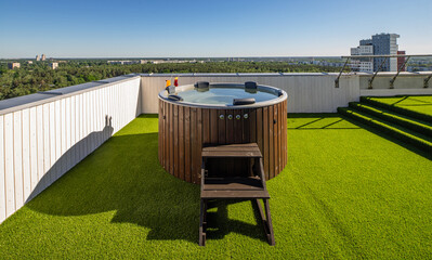 Wooden hot tub on outdoor terrace in luxury apartment. View of city.