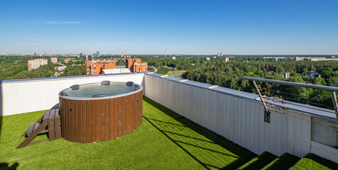 Wooden hot tub on outdoor terrace in luxury apartment. View of city.
