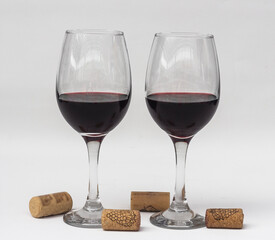 Dos copas de vino tinto y corchos sobre fondo blanco