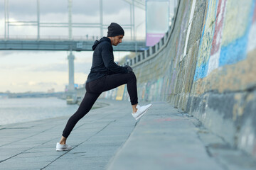 Young european runner stretching at city quay