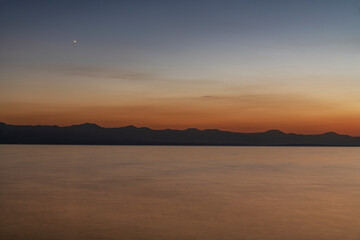 Beautiful sunset on the lake with silhouette mountais, long exposure water.