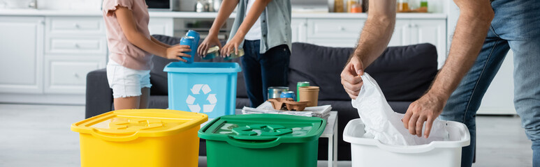 Cropped view of family sorting garbage in trash bins with recycle sign, banner