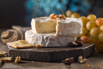 Organic homemade camembert or brie cheese on a wooden board with grapes and nuts and honey.