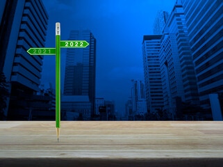 2022 and 2021 direction sign plate with green pencil on wooden table over modern office city tower and skyscraper, Business happy new year planning concept