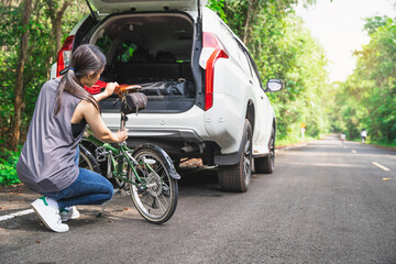 Woman taking her bicycle out from the trunk of a car. Family car with small kids bicycles rack, ready for travel. Women are cycling road bike in the morning.She is on a forest road. Healthy lifestyle.