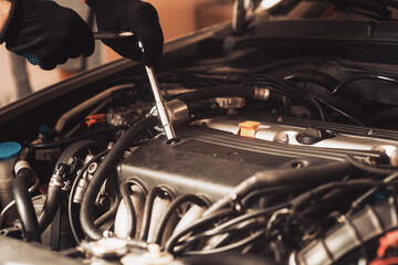 Auto mechanic repairs car. The employee carries out maintenance of the machine and shines a lamp under the hood. Operation of a mechanic under the hood of a car