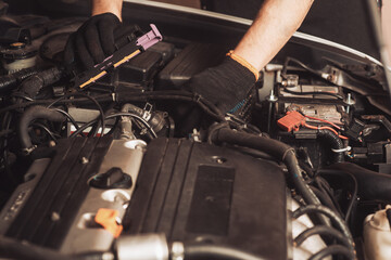 Auto mechanic repairs car. The employee carries out maintenance of the machine and shines a lamp under the hood. Operation of a mechanic under the hood of a car