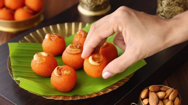 Woman eating Rava Laddu Kesar laddu motichoor Semolina Ladoo Indian sweet mithai 4K footage video Diwali Dussehra Holi Ram Navmi Ganesh chaturthi festival dessert snack golden plate Mumbai India 