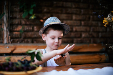 Obraz premium A cute boy in the village sits on a bench. Grandson on vacation. Spring flowers on the table.