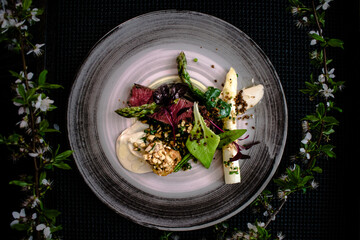 Dish of ostrich steak with white and green asparagus, garden greens and sauce on a plate on wooden table in a restaurant
