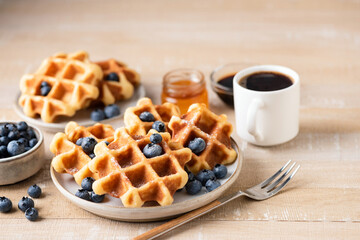 Belgian waffles with blueberries and a cup of black coffee on wooden table, breakfast in cafe