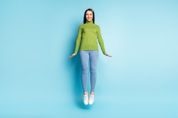 Photo of positive cheerful lady jump have fun shy pose wear green turtleneck isolated on blue...