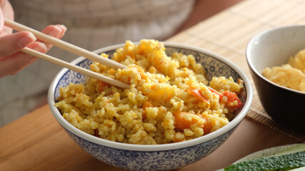 Saffron rice pilaf in bowl. Eating yellow carrot rice with spices with wooden chopsticks. Asian, indian cuisine food