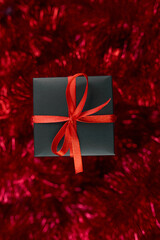 Christmas black gifts box on red tinsel background, abundant decor,  Flat lay, top view, from above, copy space. Merry Christmas, Happy New year..