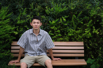 Fototapeta premium Asian young man sitting in park bench looking at camera