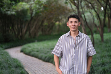 one Asian young man smiling and looking at camera in natural green park