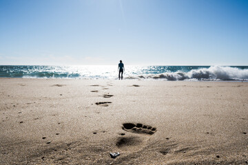 Footprint in the sand of the beach with a out of focus person at the ocean