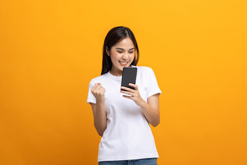 Pretty young asian woman using smartphone standing on isolated yellow background feeling happy....